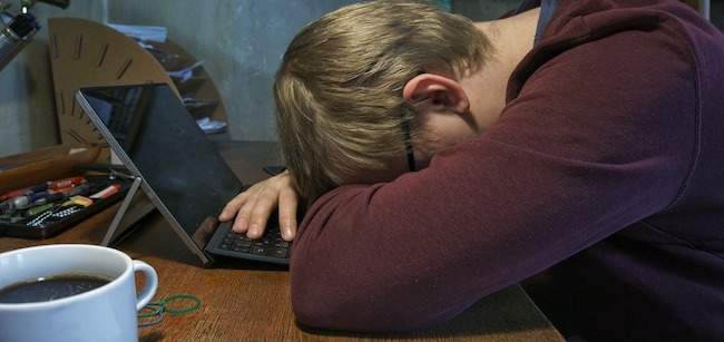 Man in front of laptop computer with his head on the table.
